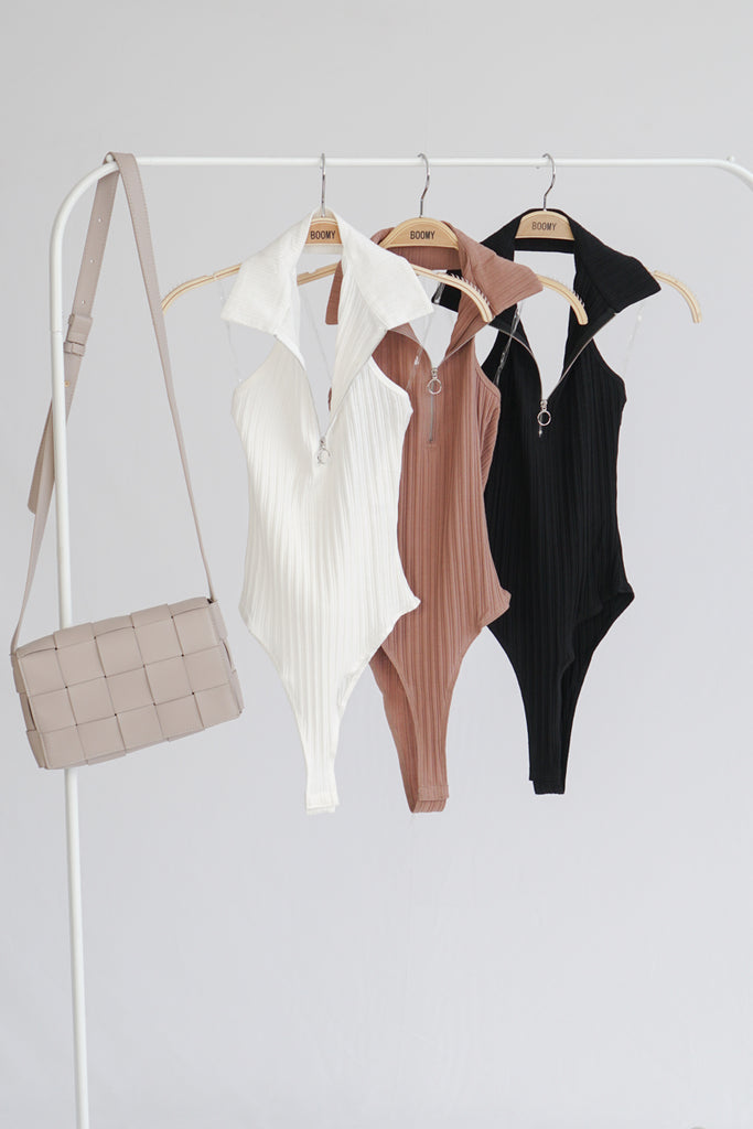 A woven knit sleeveless ribbed bodysuit featuring a collar, a zip-up with ring, an open back and button snaps on the bottom for closure.
