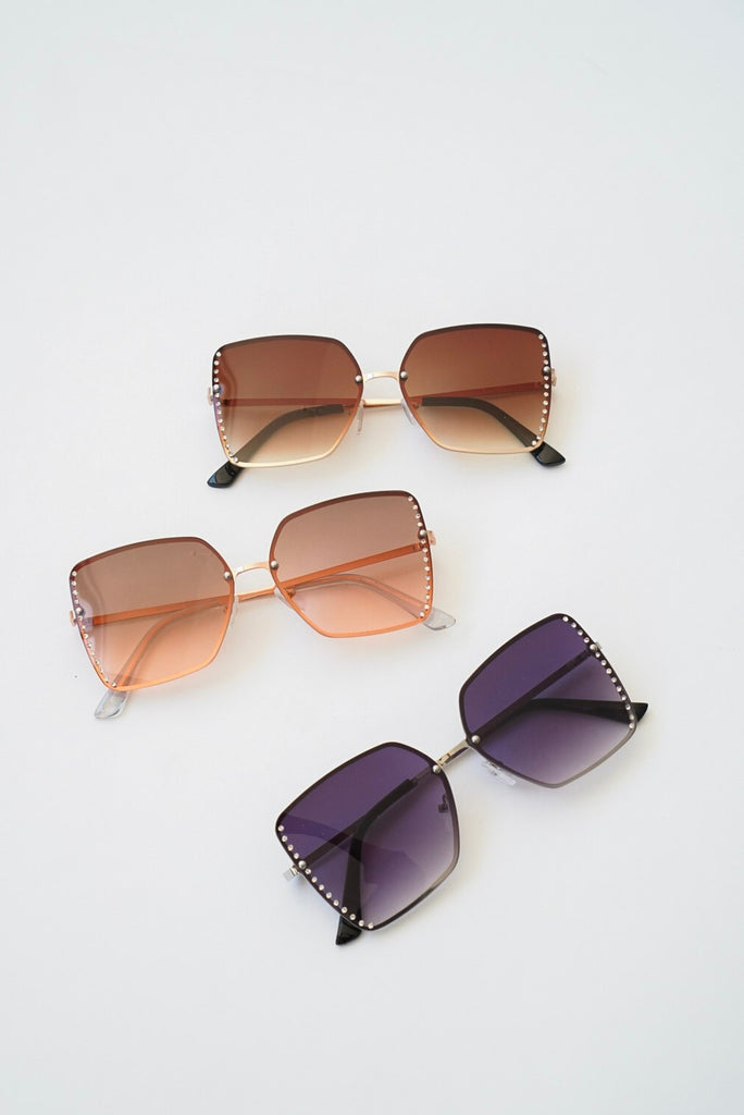 A pair of square tinted framed sunglasses featuring rhinestones on the sides for design.