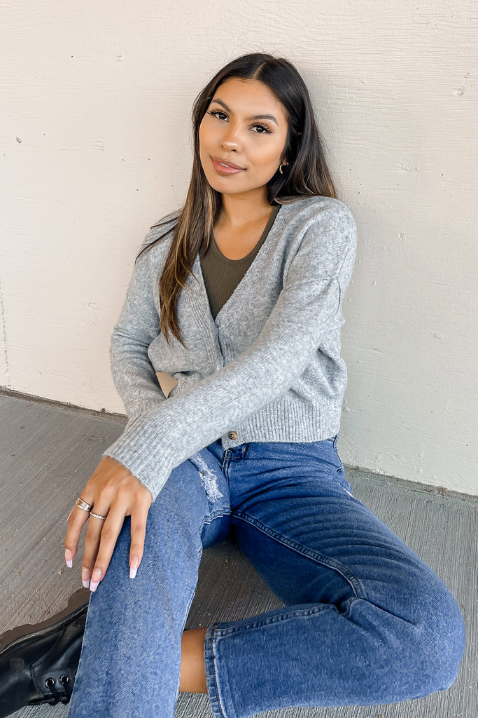 A gray oversized, cropped knit cardigan featuring a V-neckline, button front, and long sleeves