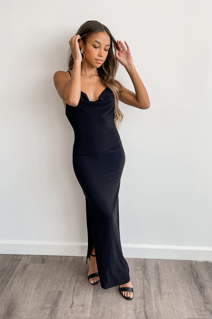 A black maxi dress featuring a cowl neck, slit on both sides, and cami straps.