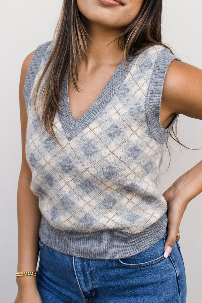 A gray woven knit sweater vest crop top featuring an allover argyle print, featuring a v-neckline and a ribbed hem.