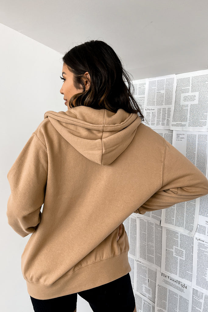 A tan long sleeve fleece jacket featuring a zip-up, drawstring hoodie and front pockets.
