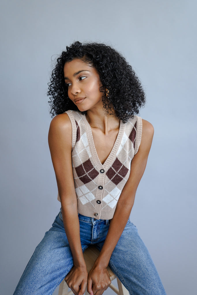 A woven knit sweater vest crop top featuring an allover argyle print, a v-neckline and buttons in the front.