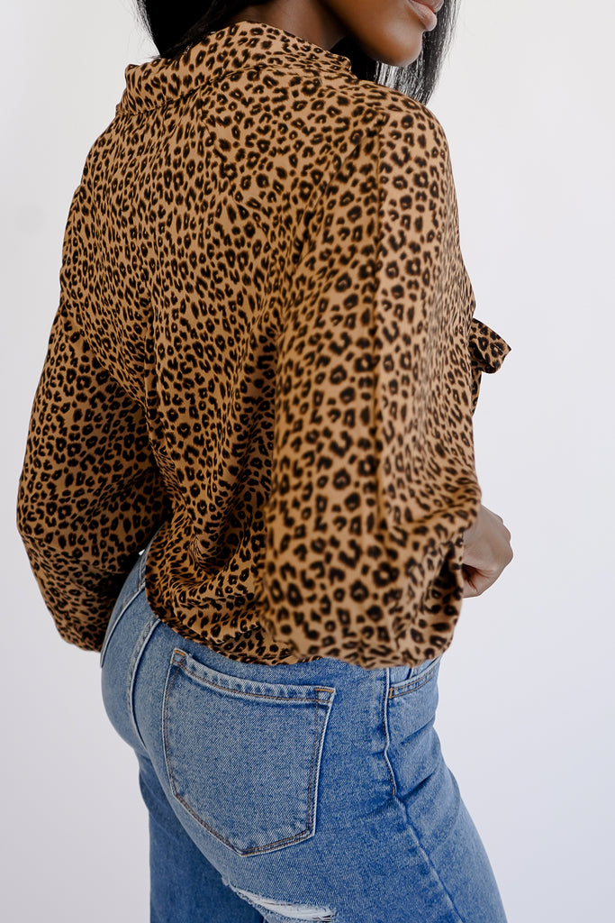 An all over cheetah print top featuring a plunging V-neckline, long sleeves with shirred accents, and front self-tie closure.