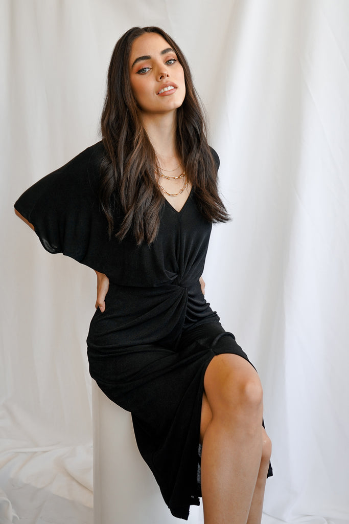 A twist dress featuring a knot detail, low v-neckline, and thigh split. Model is wearing a size Small.