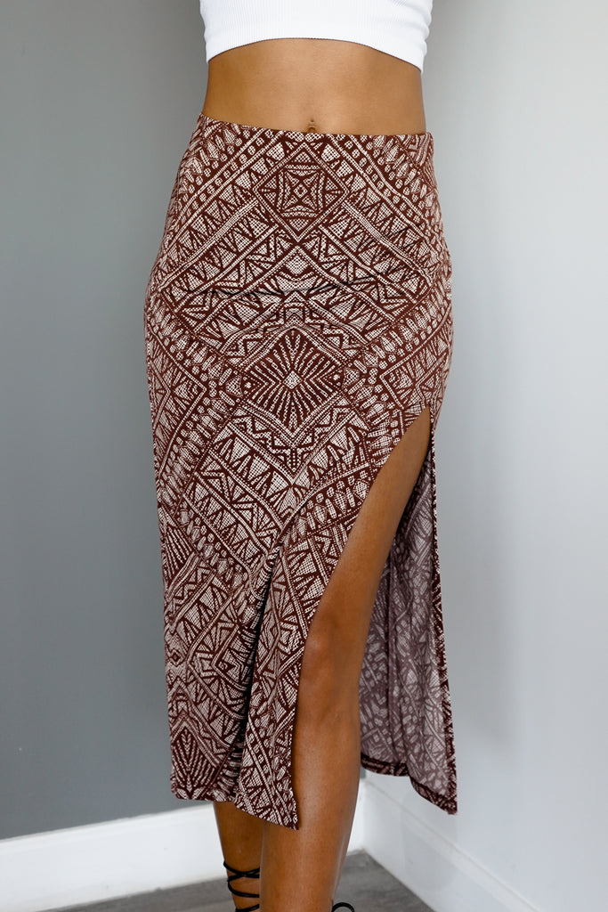 A midi skirt featuring a straight silhouette, knee length, leg slit, and a elastic waist.