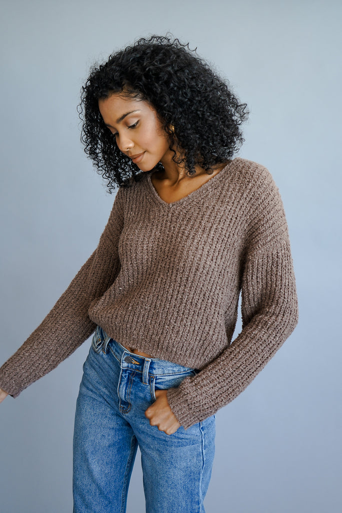 A fuzzy knit sweater featuring a ribbed construction, V-neckline, long sleeves, and a cropped hem.