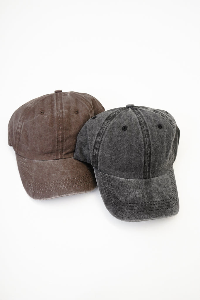 A woven dad cap featuring an oil wash, curved brim, eyelets, button top, and adjustable backstrap with burnished metal hardware.