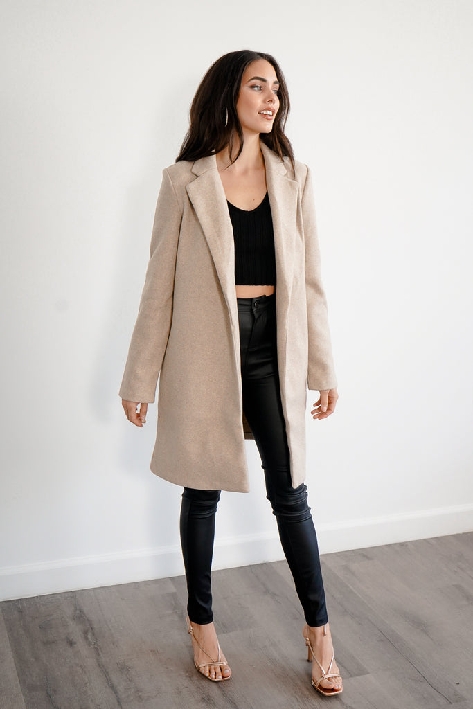 A woven coat featuring notched lapels, dropped long sleeves, front slanted pockets, a longline silhouette, and an open front.
