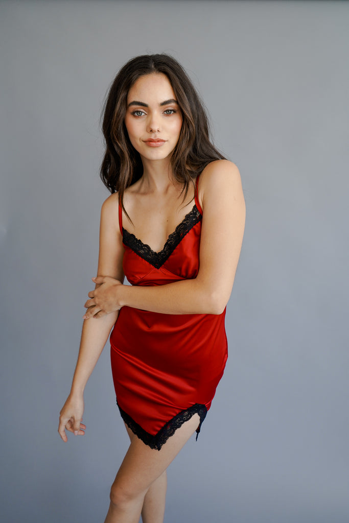 A satin mini dress featuring lace trim, V-neckline, cami straps, a straight-cut back, front slit, and a bodycon silhouette.