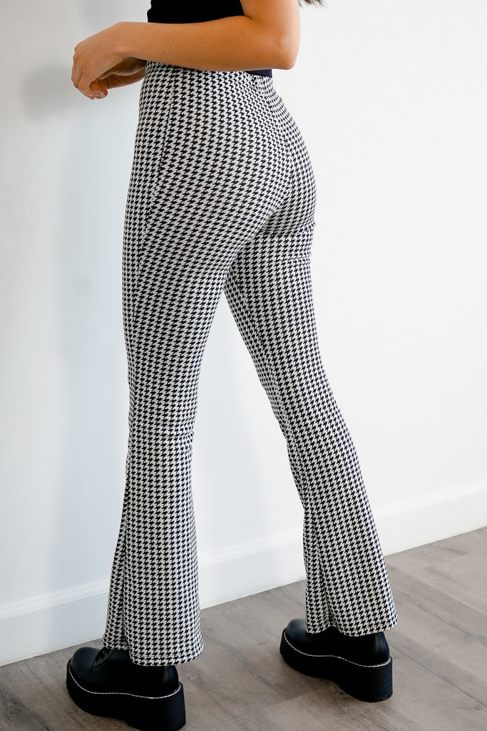 A pair of woven pants featuring an allover hounds tooth pattern, high-rise waist, and flare leg.
