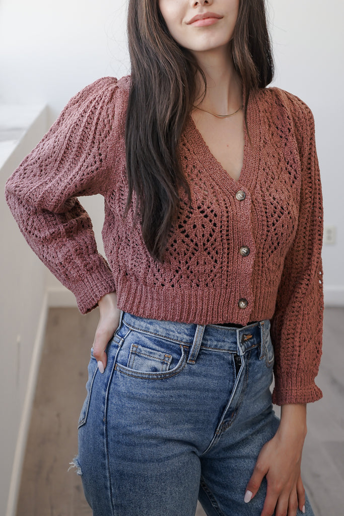 A cropped knit cardigan featuring a V-neckline, button front, and long sleeves.
